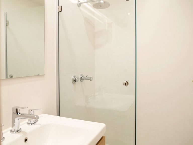 Bright, clean attached bathroom with modern white fixtures, sparkling chrome taps, and spotless glass shower area