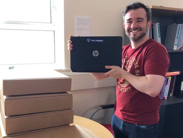 A smiling man holds up a donated refurbished laptop 