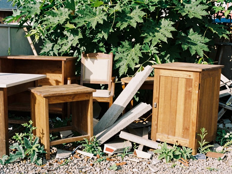 Before: Cluttered side yard filled with old wooden furniture, broken concrete pieces, and wild weeds growing through gravel, 35mm