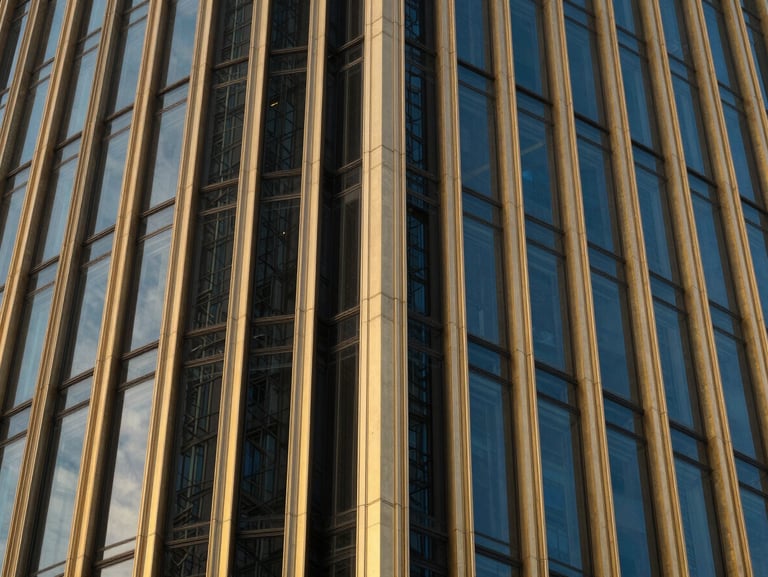 Close-up architectural crop of a luxury commercial tower facade, gold steel frames, dark glass panels, dramatic evening lighting