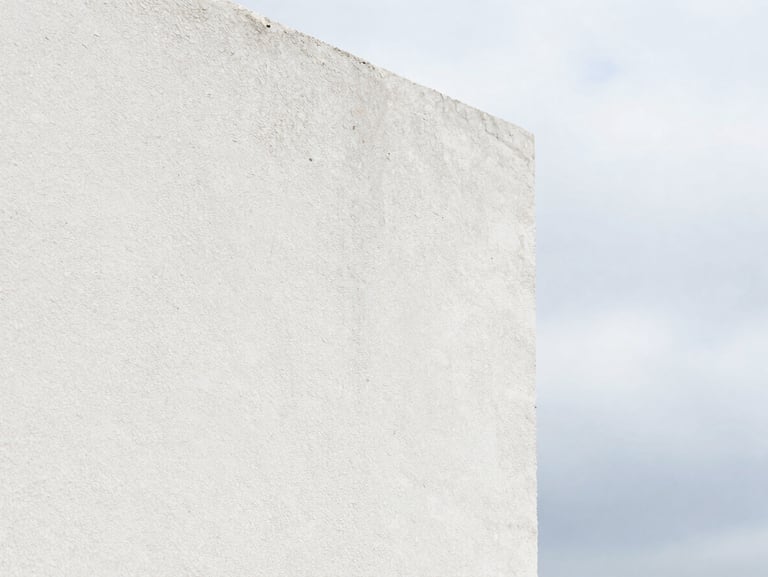 Macro shot of white crépi taloché texture, showing fine mineral grains, soft side lighting emphasizing the pattern, architectural detail.