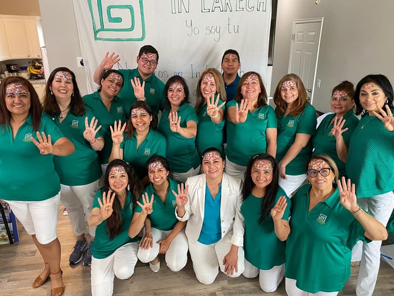 A diverse group of community volunteers in green shirts pose with face paint for an In Lak’Ech event.
