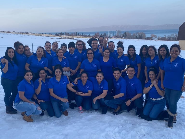 A diverse group of coworkers in blue shirts posing for a team photo in the snow with a lake view.