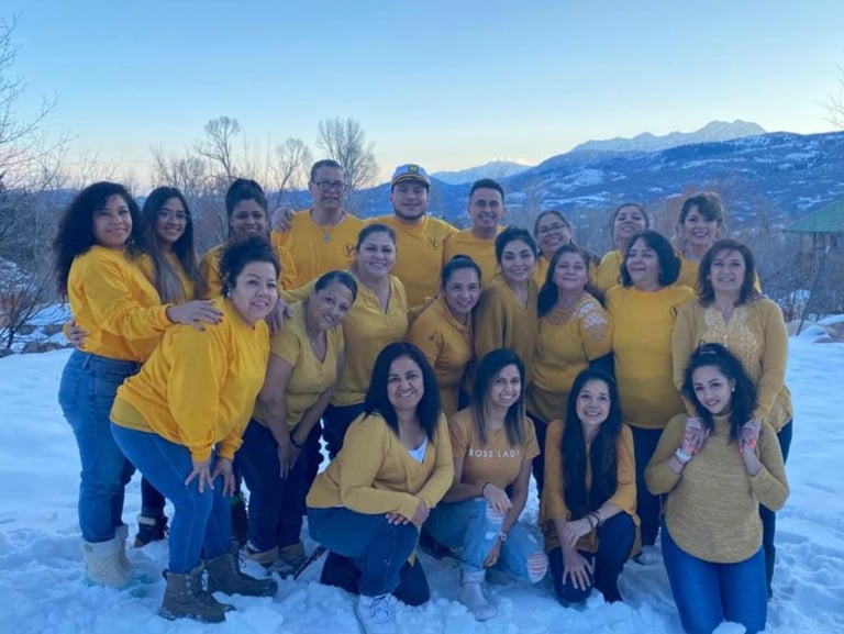 A group of diverse people in yellow shirts posing together in the snow with mountain scenery.