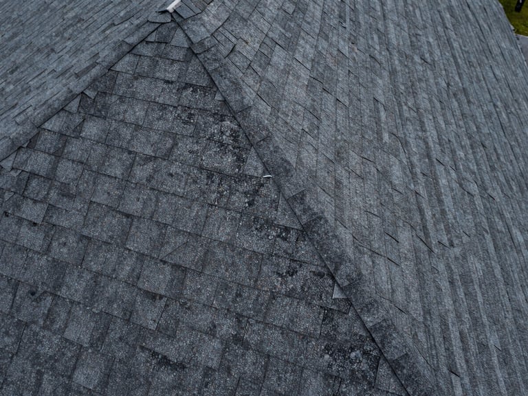 Close aerial of a residential asphalt shingle rooftop, granule wear and flashing detail visible, overcast diffused daylight eliminating harsh shadows, drone framing tight to roofline