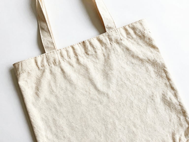 Bright high-key product photography of a custom canvas tote bag flat-lay showing precise stitching details on a clean white background, 50mm