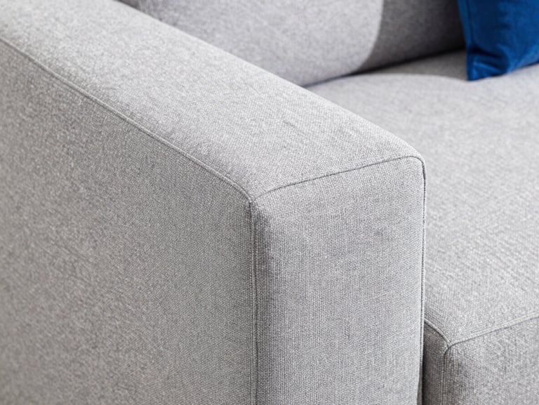 Macro shot of a clean light grey fabric sofa, showing deep fiber texture, bright natural light, professional commercial photography.