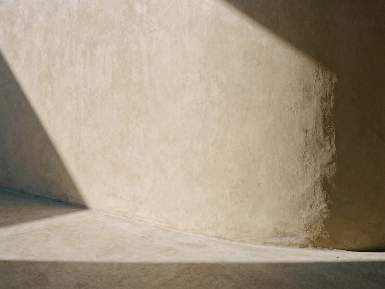 Close-up of a curved plaster wall meeting a concrete floor, soft natural daylight casting long architectural shadows, warm editorial photography, 35mm film texture.