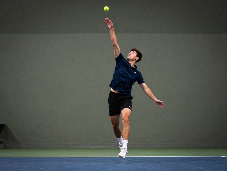 An adult player mid-air executing a focused serve on an indoor court, crisp illumination