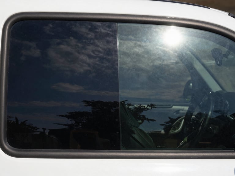 High-contrast split screen showing a vehicle window half tinted with deep charcoal film and half untinted, showing dramatic glare reduction under bright sunlight