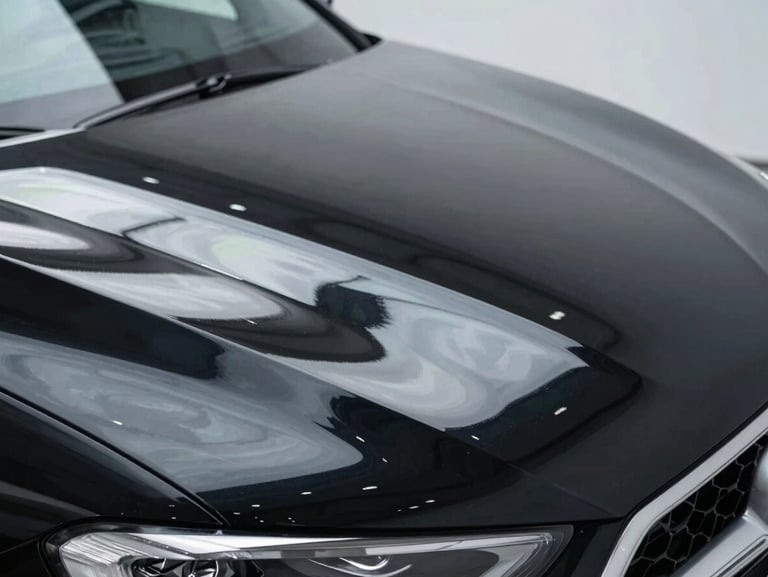 Close-up of the same black car hood after multi-stage paint correction, deep mirror-like gloss reflecting a clean overhead light perfectly, premium automotive photography