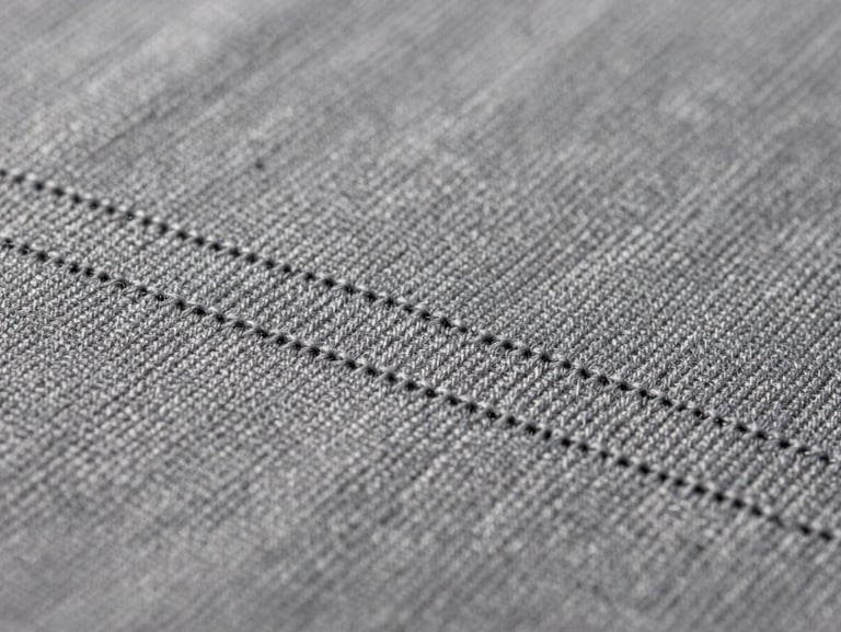 Macro close-up of precise, tight embroidery stitching on heavy slate gray cotton fabric, showing the rich weave and clean thread lines under studio light.