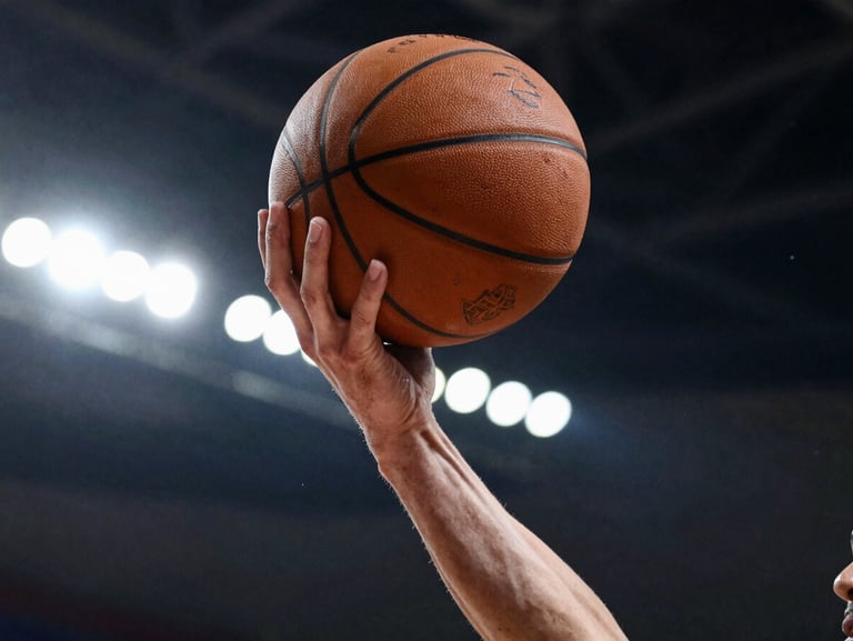 Low-angle action shot of a player mid-drive under dramatic stadium lighting, hand gripping a worn basketball, high-contrast shadows.