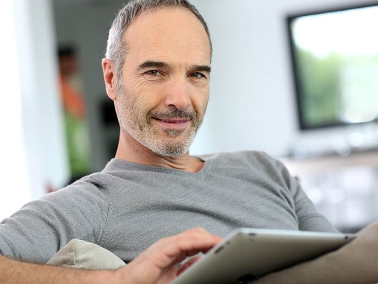 a man sitting on a couch with a tablet computer Martin PE / COACH