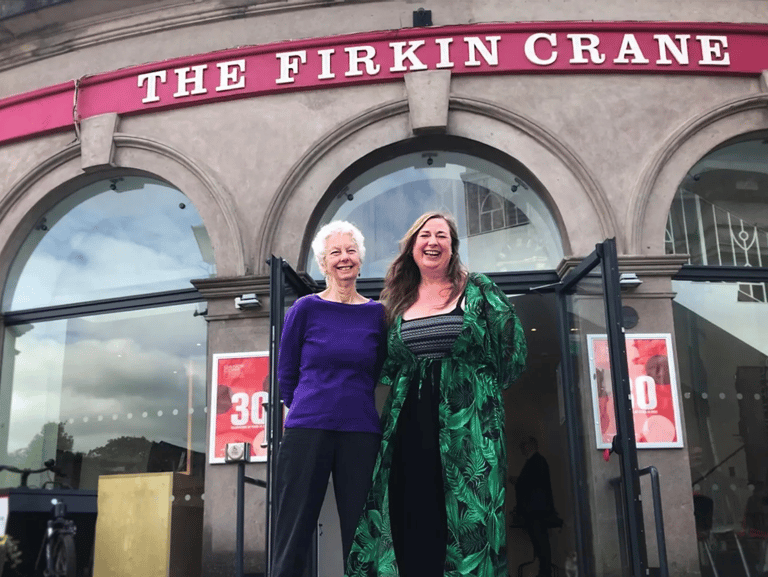 two women standing in front of a building that has a sign saying The Firkin Crane