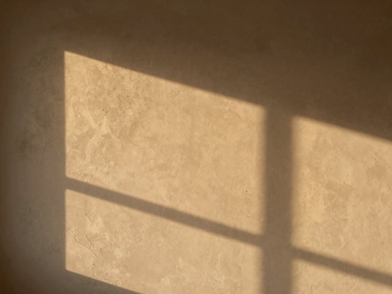 Wide environmental interior shot of a finished wall with clayxible texture, warm golden-hour light raking across the surface revealing subtle depth and tone variation, no people, no furniture clutter