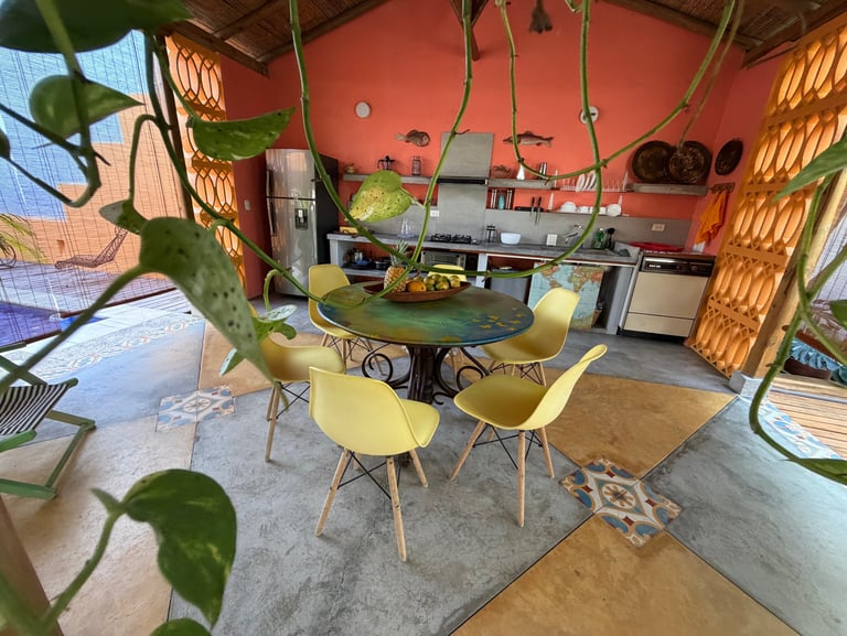 Rustic open-air kitchen with yellow mid-century chairs, a round table, and coral walls.