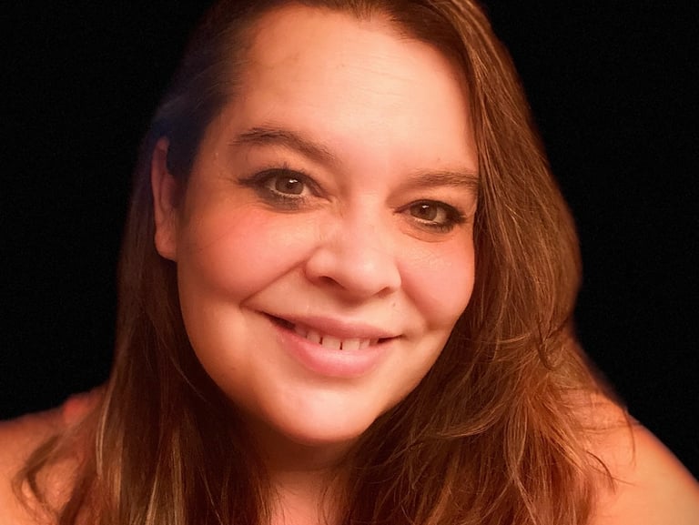 A smiling middle-aged woman with long brown hair against a dark background.