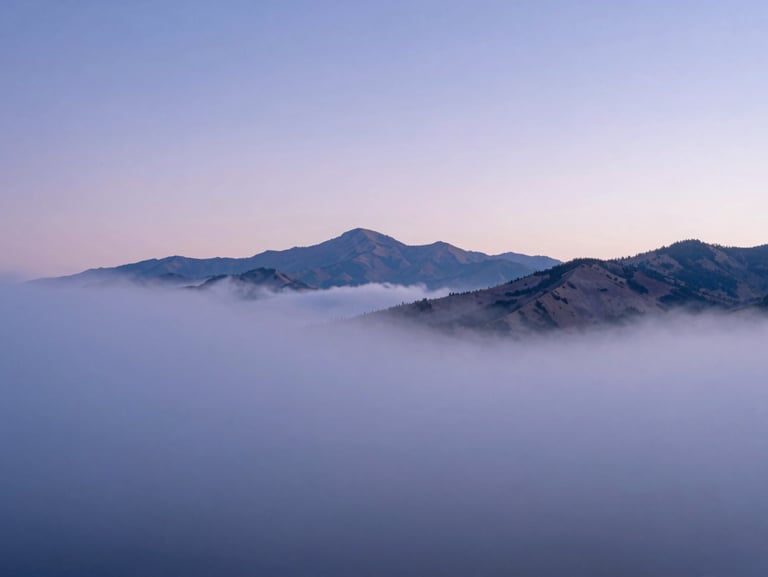 Soft-focus view of misty Utah mountains at dawn, light blue and lavender hues filtering through low-hanging clouds, quiet and expansive landscape.
