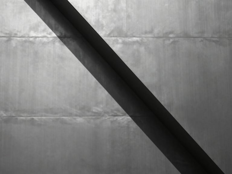 Abstract geometric composition of brushed steel panels intersecting, sharp focus, hard sunlight reflections, desaturated monochrome tones.