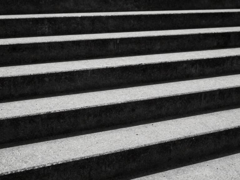 Extreme close-up of raw concrete architectural stairs under harsh, high-contrast sunlight with deep black shadows, 35mm, monochrome desaturated tones.