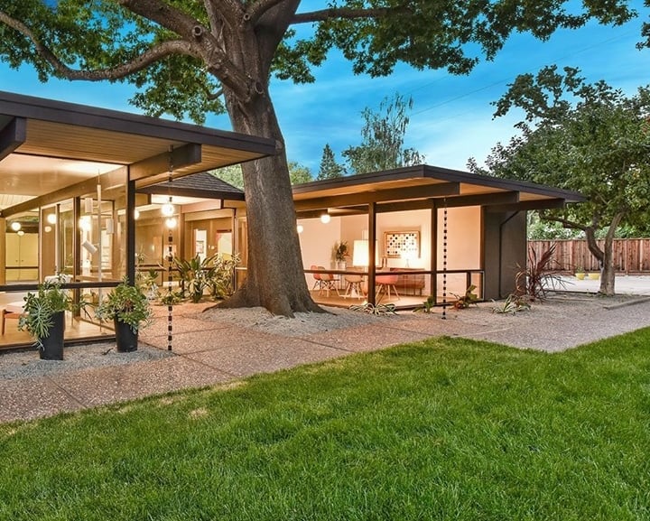 Santa Ynez Valley home with glass walls, flat roof, and a large oak tree in a lush green backyard.