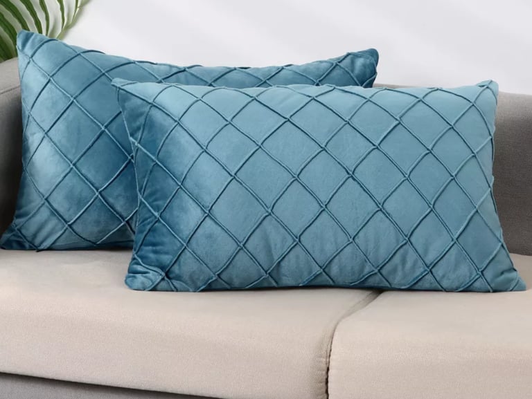Pair of teal blue velvet lumbar throw pillows with a diamond quilted pattern on a gray sofa.