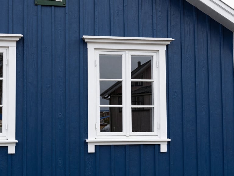 A freshly painted deep blue wooden house wall in Vadsø, clean white trim, immaculate finish under crisp daylight
