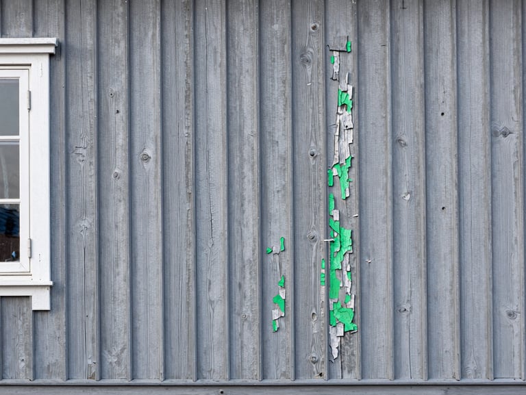 A weathered, peeling wooden house wall in Vadsø before painting, grey and worn by Arctic wind