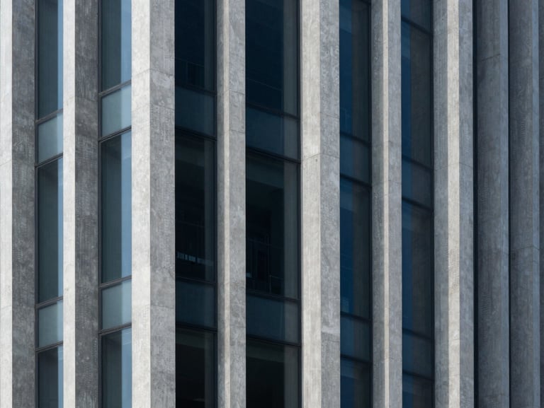 Abstract architectural geometry of a modern concrete and glass building facade, clean vertical lines, deep shadows, cool blue and slate tones.