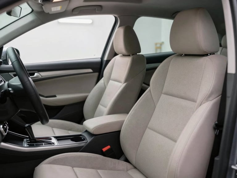 Interior of a car with seats and door panels being dry cleaned using equipment, bright workshop lighting from overhead, close view showing the cleaning process on fabric upholstery