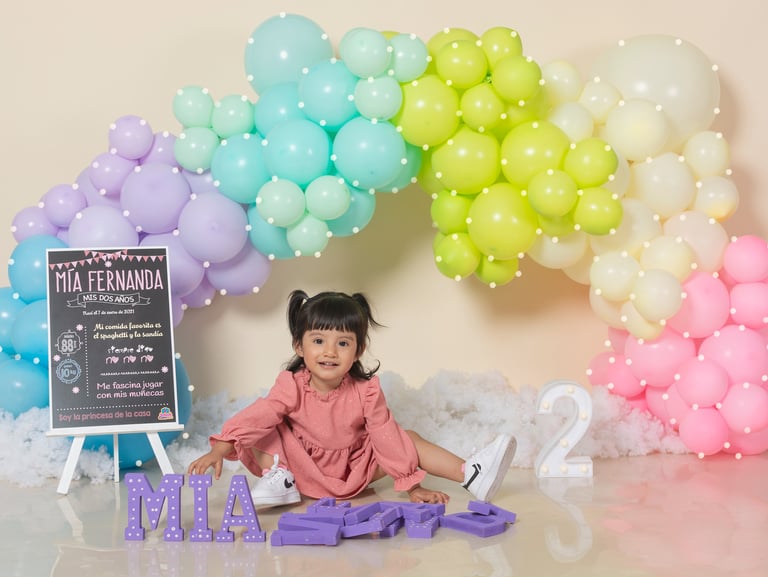 a baby girl sitting on a table with balloons and balloons