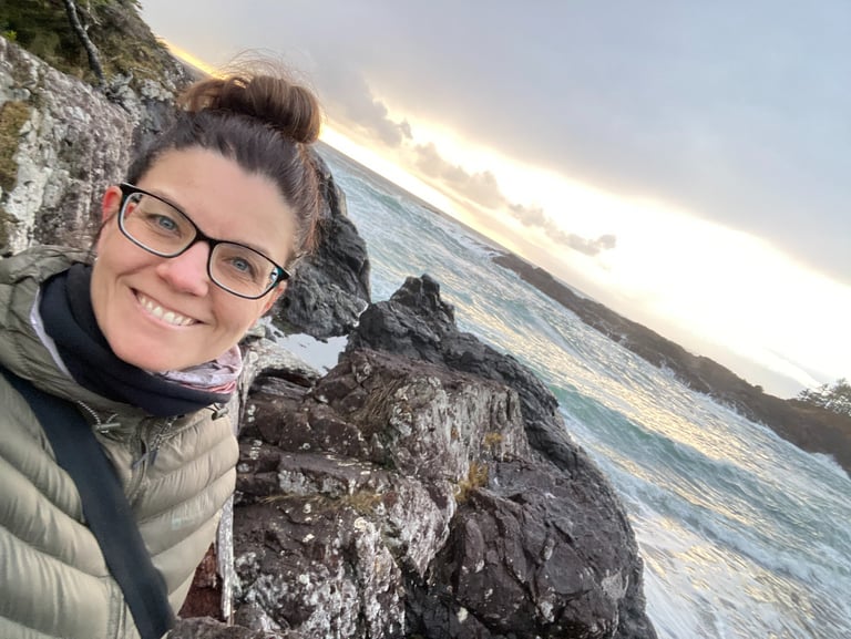 The founder of Alignment Era Consulting smiling on a rocky coast at sunset with ocean waves.