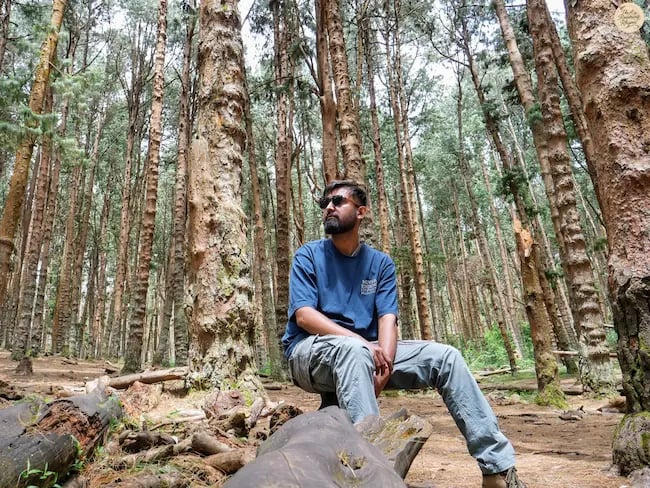 Traveler posing in Kodaikanal pine forest, surrounded by tall pine trees and serene charm.