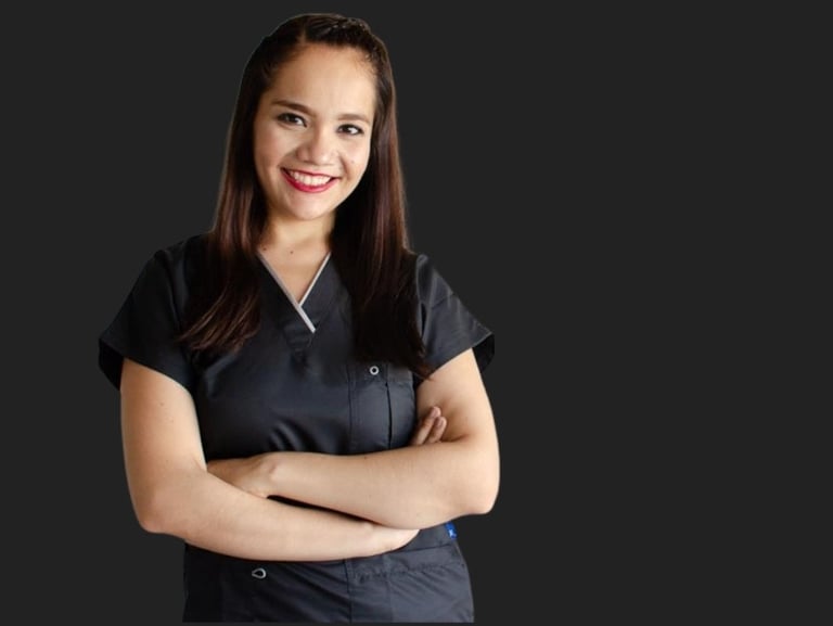 Smiling female medical professional in dark grey scrubs with arms crossed against a black background.