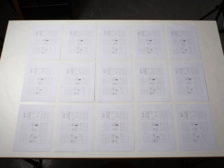 Bird's-eye view of a studio workstation, a grid of printed layout sheets arranged in precise rows on a matte white surface under studio strobe lighting, no hands or people visible