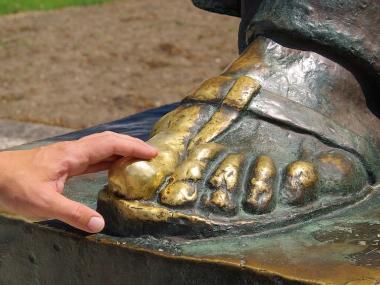 Close-up of a hand touching the golden toe of the Grgur Ninski statue in Split for good luck