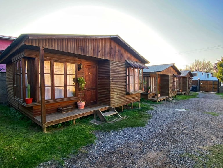 Rustic wooden cabins and vacation cottages along a gravel path under a clear blue sky.