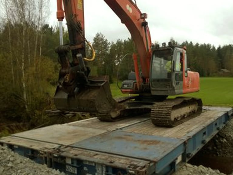 Two blue 40ft flat racks side by side as a bridge with a large trac hoe parked on top