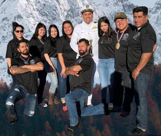 A group of friends posing in front of a mountain backdrop with a man in a white naval uniform.