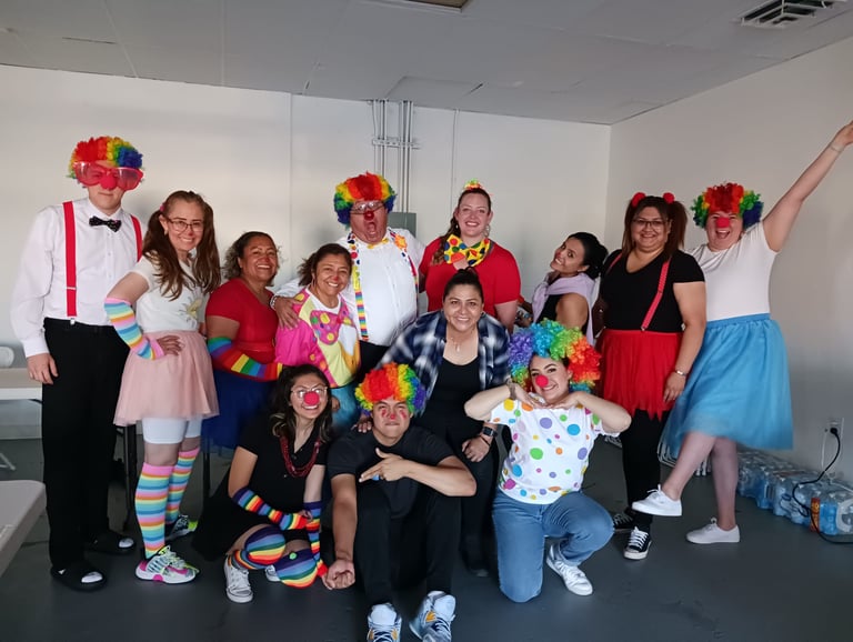 A diverse group of people posing in colorful clown costumes with rainbow wigs and red noses.