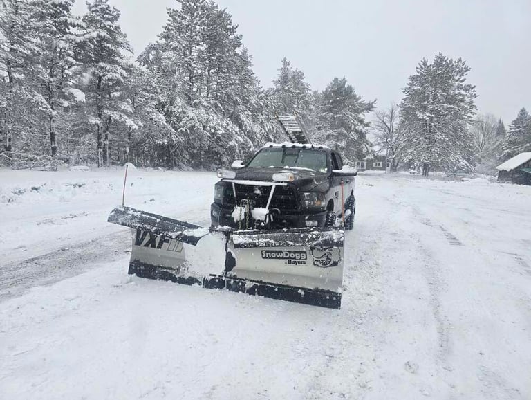 A black pickup truck with a SnowDogg v-plow clearing deep snow on a winter driveway.