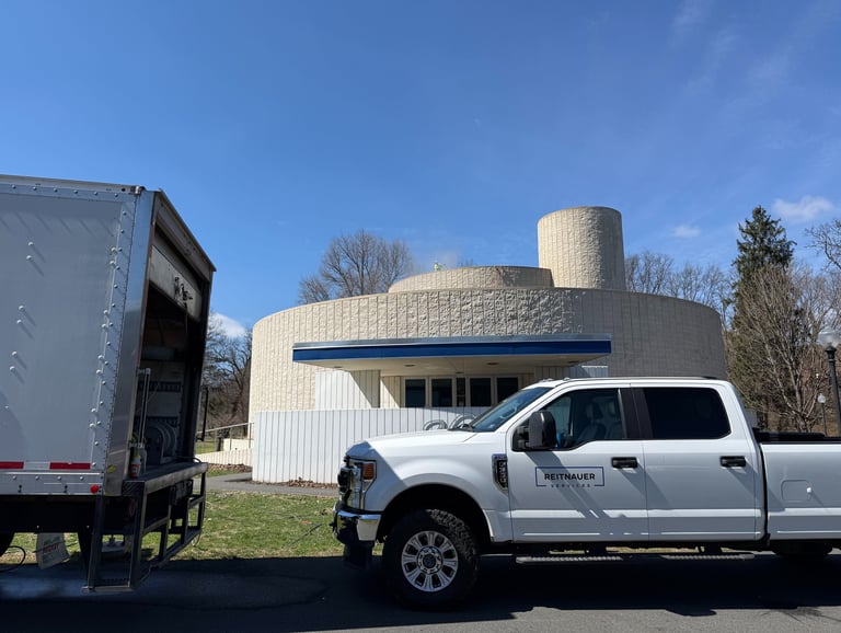 Reitnauer Services white Ford pickup truck parked next to a service box truck near a circular stone building.