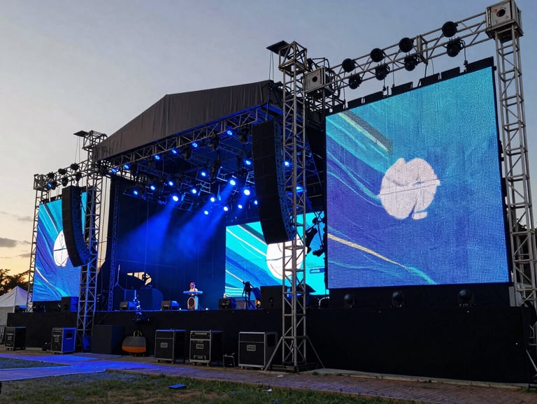 Professional photography of a large outdoor stage setup at sunset in Brazil, featuring high-end audio equipment and massive LED screens, steel blue atmospheric lighting.