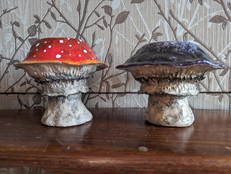 Hand-painted red amanita and purple clay mushroom figurines on a wooden shelf.
