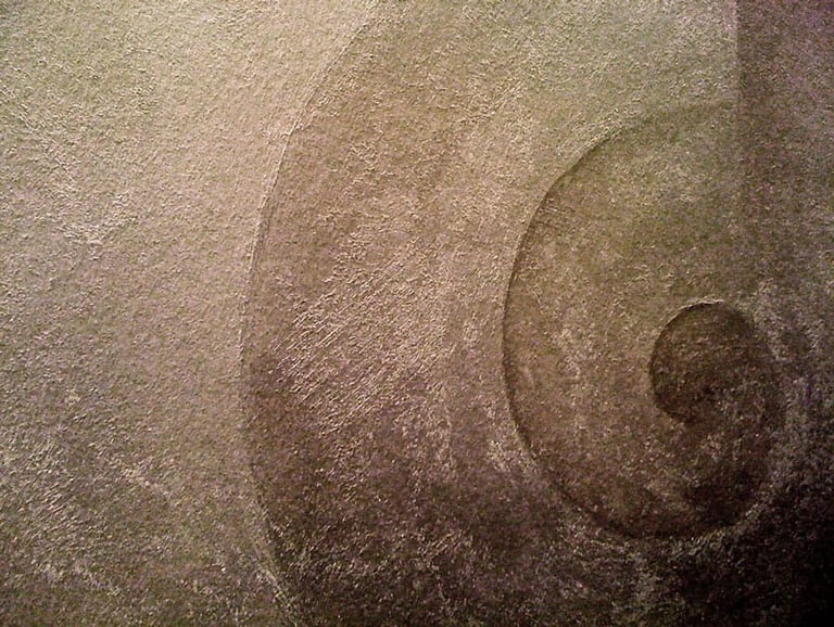 Close-up of a snail swirl painted with warm silver paint in a gritty texture.