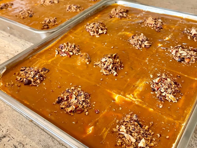 Two baking trays filled with homemade pumpkin bars topped with caramel glaze and chopped pecans.