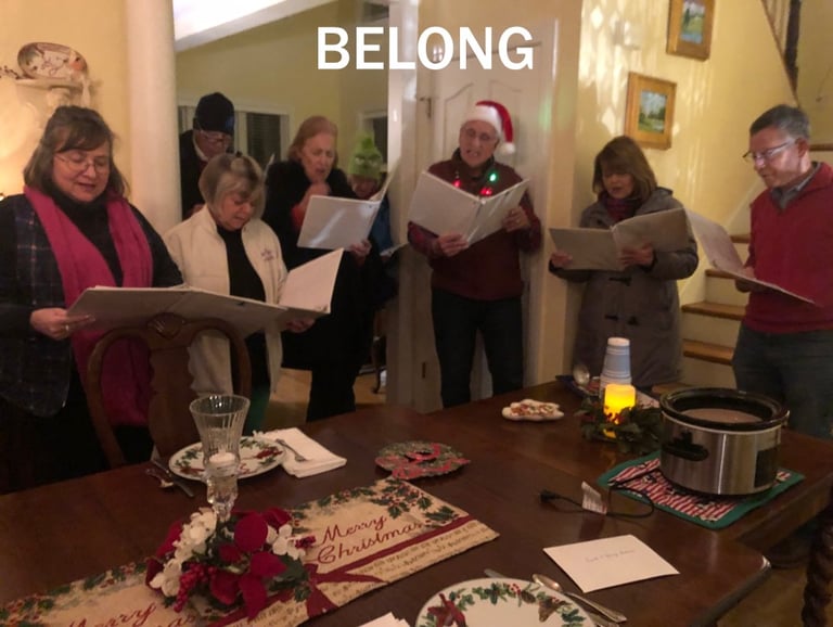 Group of seven adults singing Christmas carols around a table.