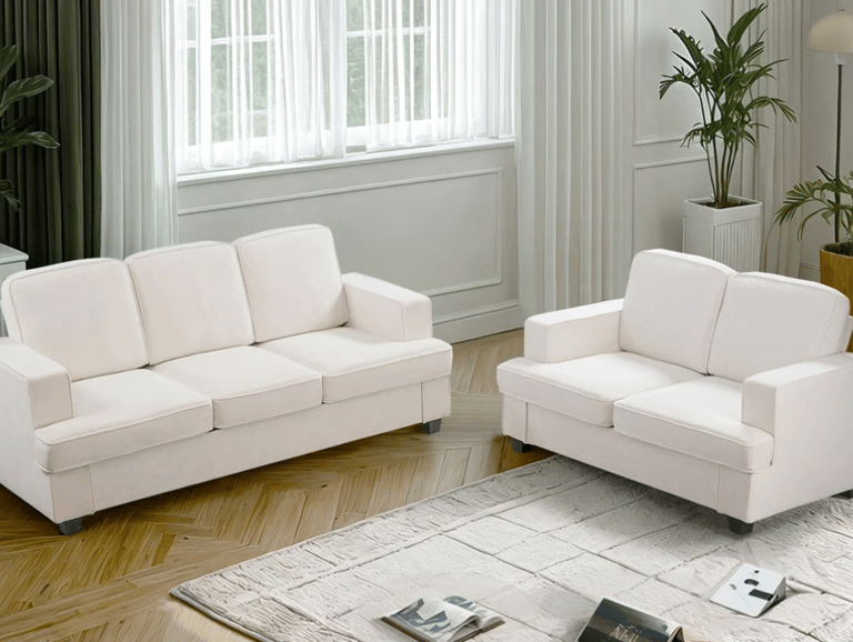 Modern white fabric sofa set and matching loveseat on a textured rug in a bright living room.