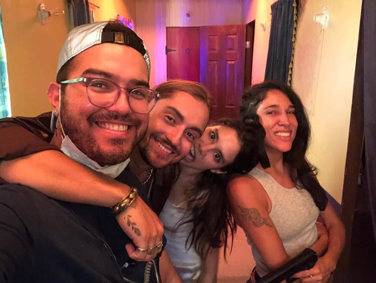 A group of four smiling friends posing for a playful selfie together indoors.